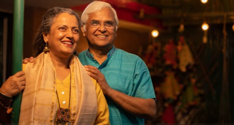 An older Indian couple standing together, looking off into the distance.