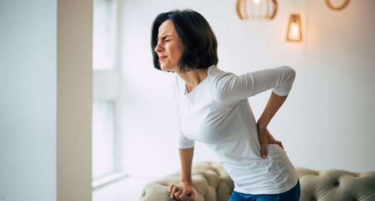 A woman in a white shirt bent over with a hand on her back, as if in pain.