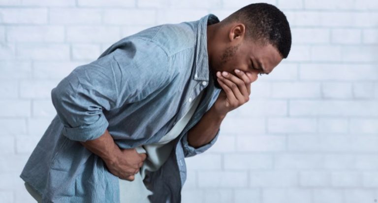 A man standing bent over, with one hand on his stomach and his other hand covering his mouth. He looks very nauseous.